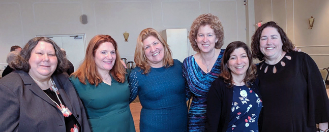 Six smiling women, standing shoulder to shoulder